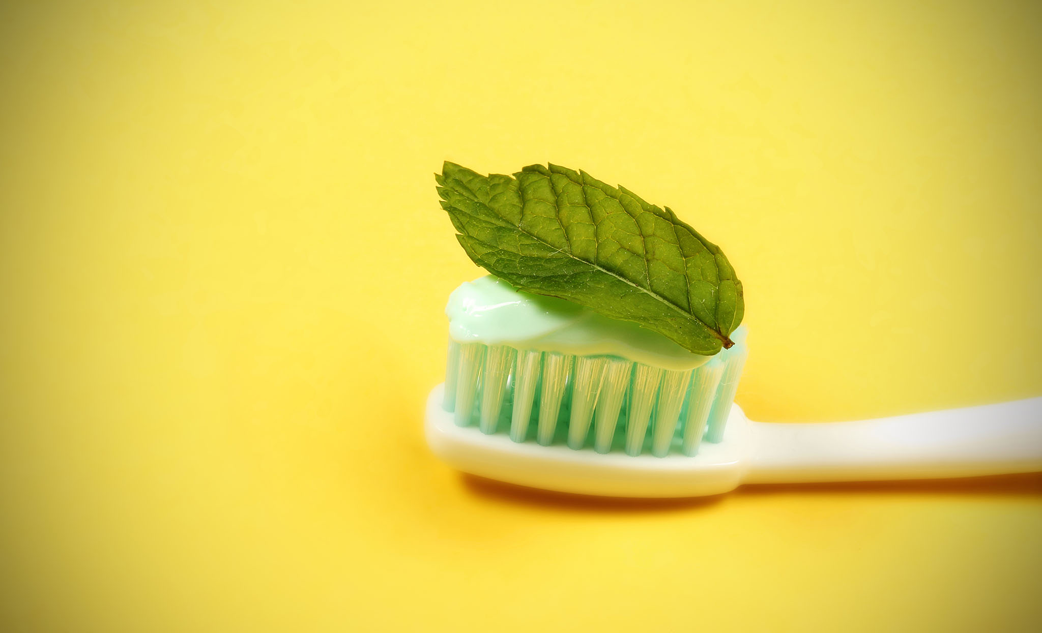 Tooth brush on a yellow background with a fresh mint leaf.